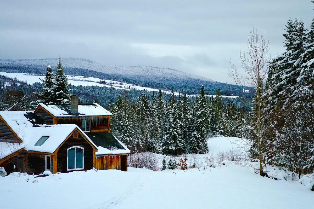 A wooden house with snow on the roof among snowy spruce trees in New Hampshire
